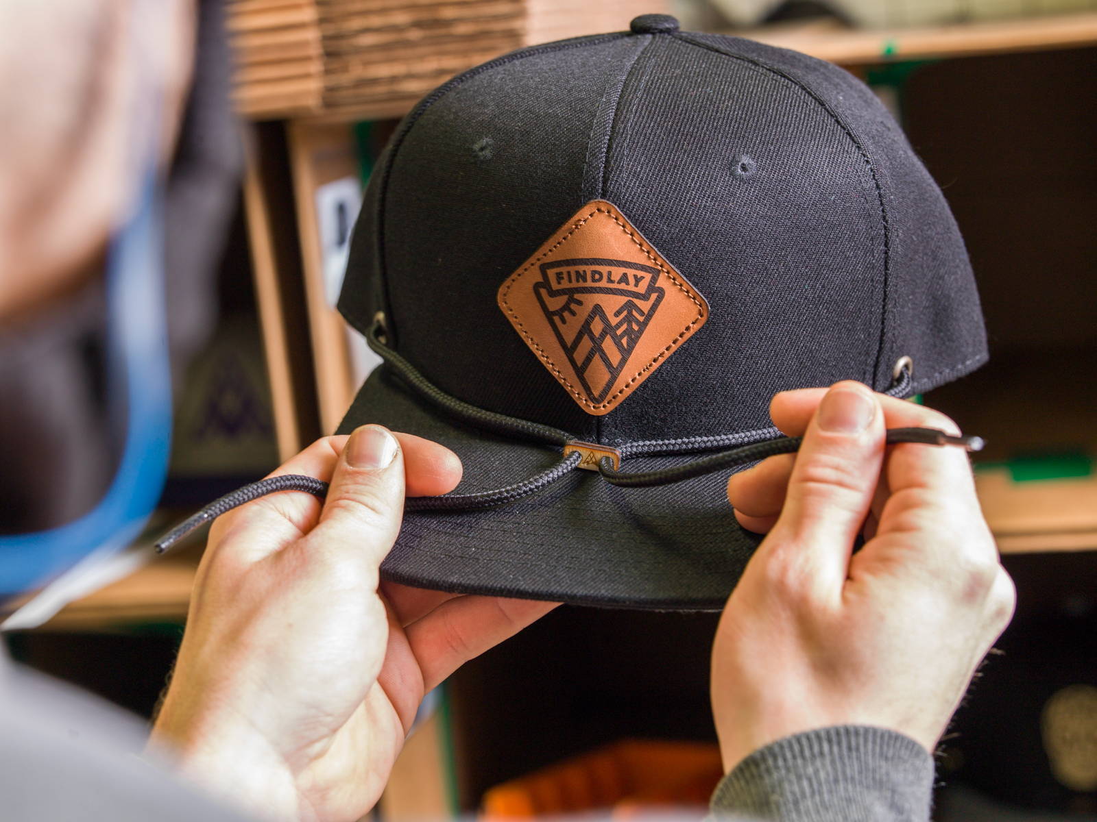 Hands tying the stampede laces on a black Findlay snapback with a leather Mt. Findlay patch.