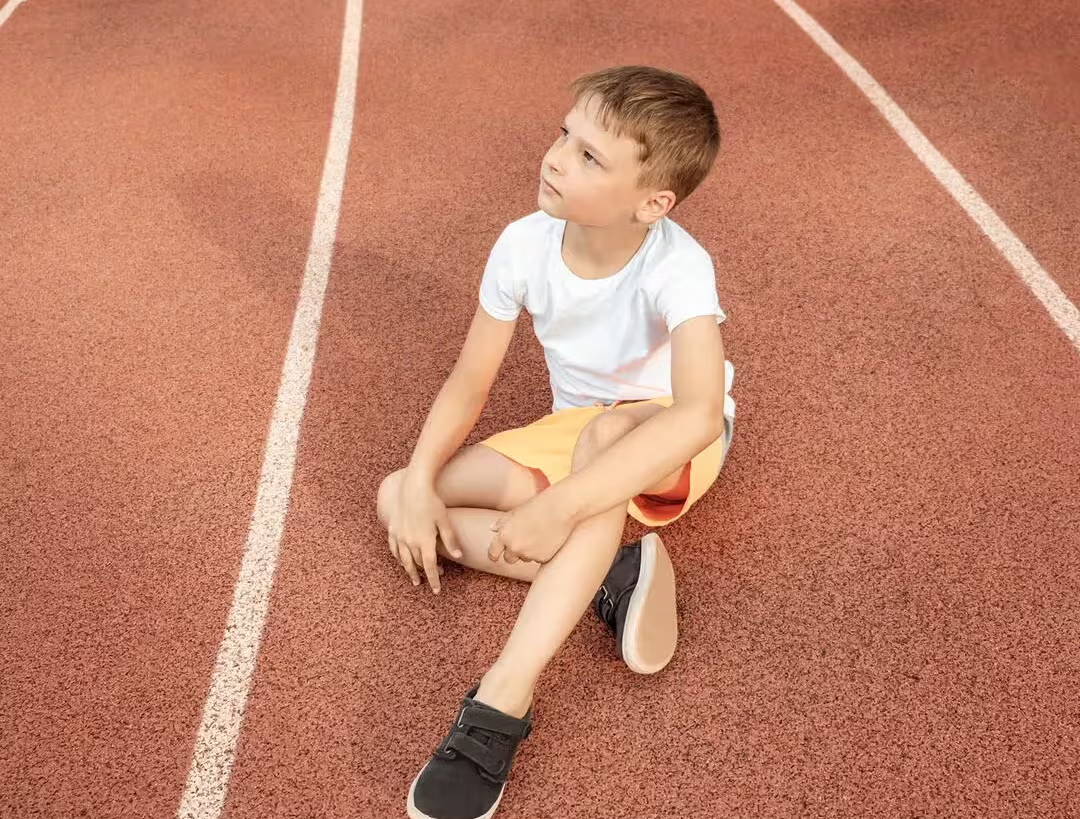 Garçon assis au milieu de la piste de course - l’exercice peut déclencher de l’asthme, il a donc peut-être dû s’arrêter ou ne peut pas participer.