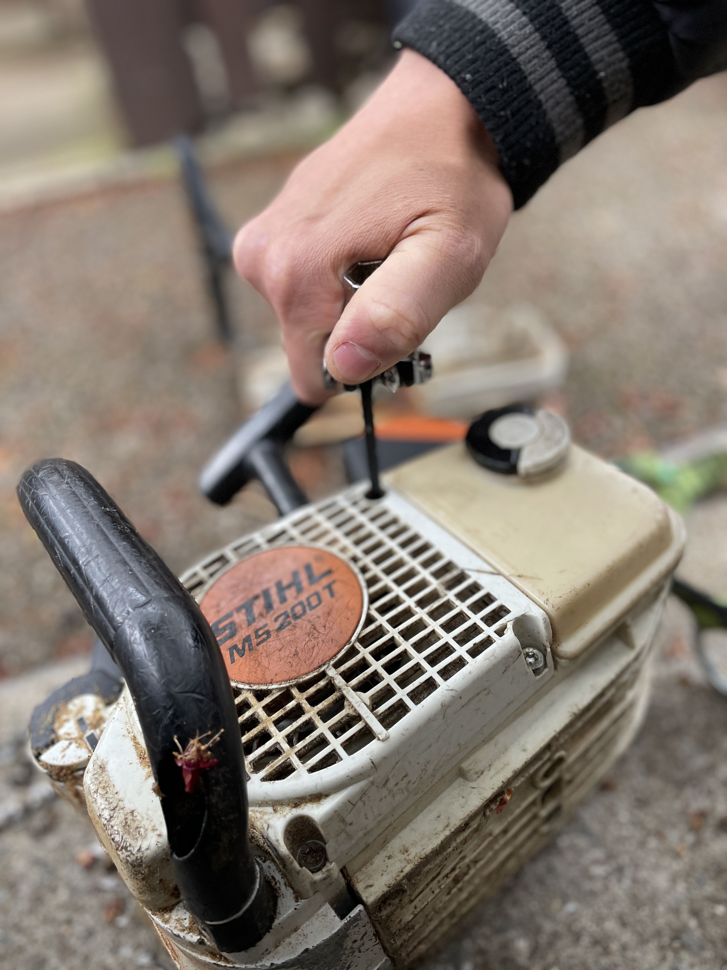 A hand adjusting a part on a gas-powered chainsaw.