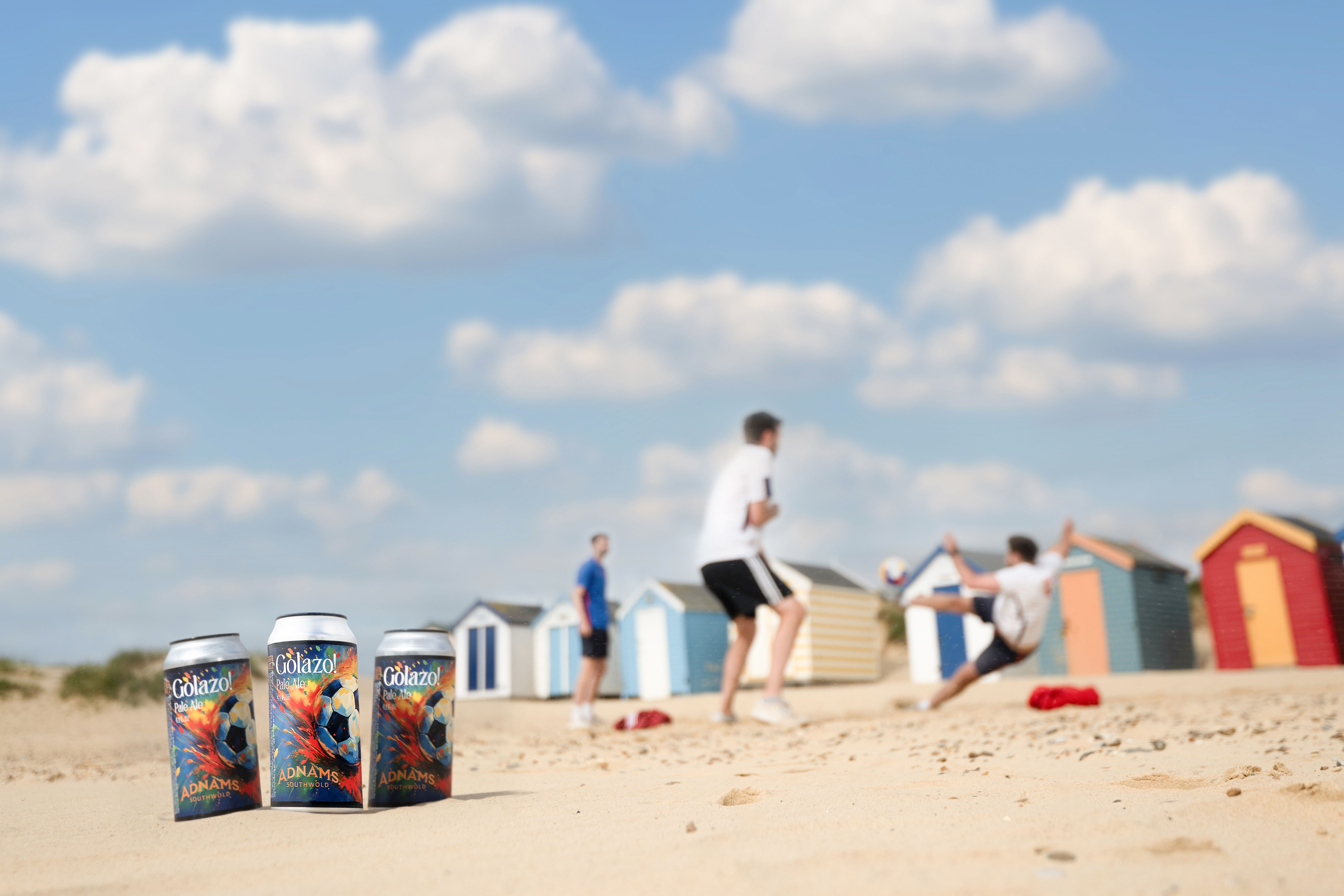 People playing on a beach with colorful beach huts in the background.