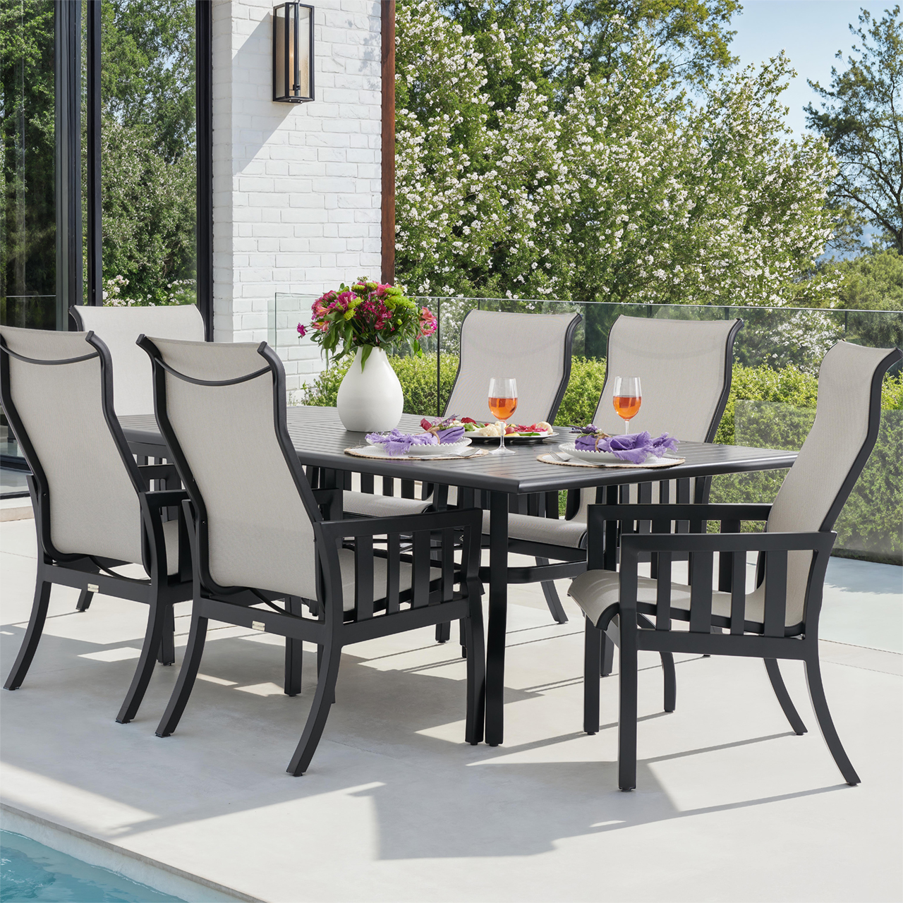 Outdoor dining set with chairs, table, and drinks near a pool.