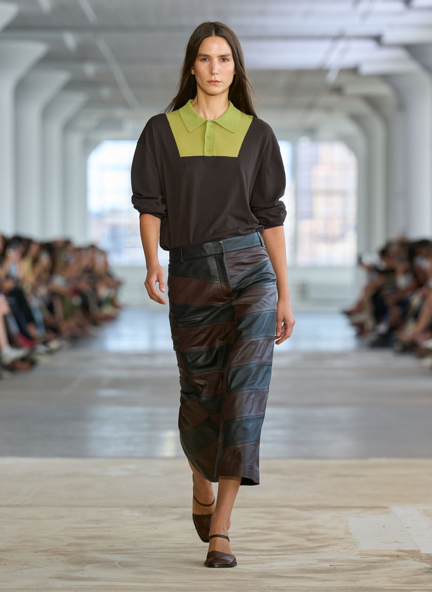 Model walking down runway wearing a black top and patterned skirt.