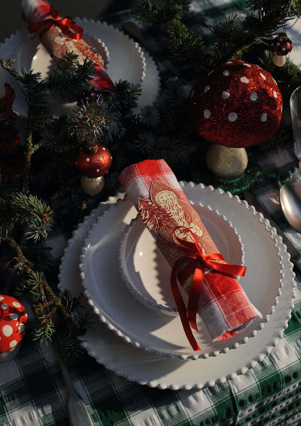 A red and white checked napkin, topped with a santa claus print tied in a ribbon.