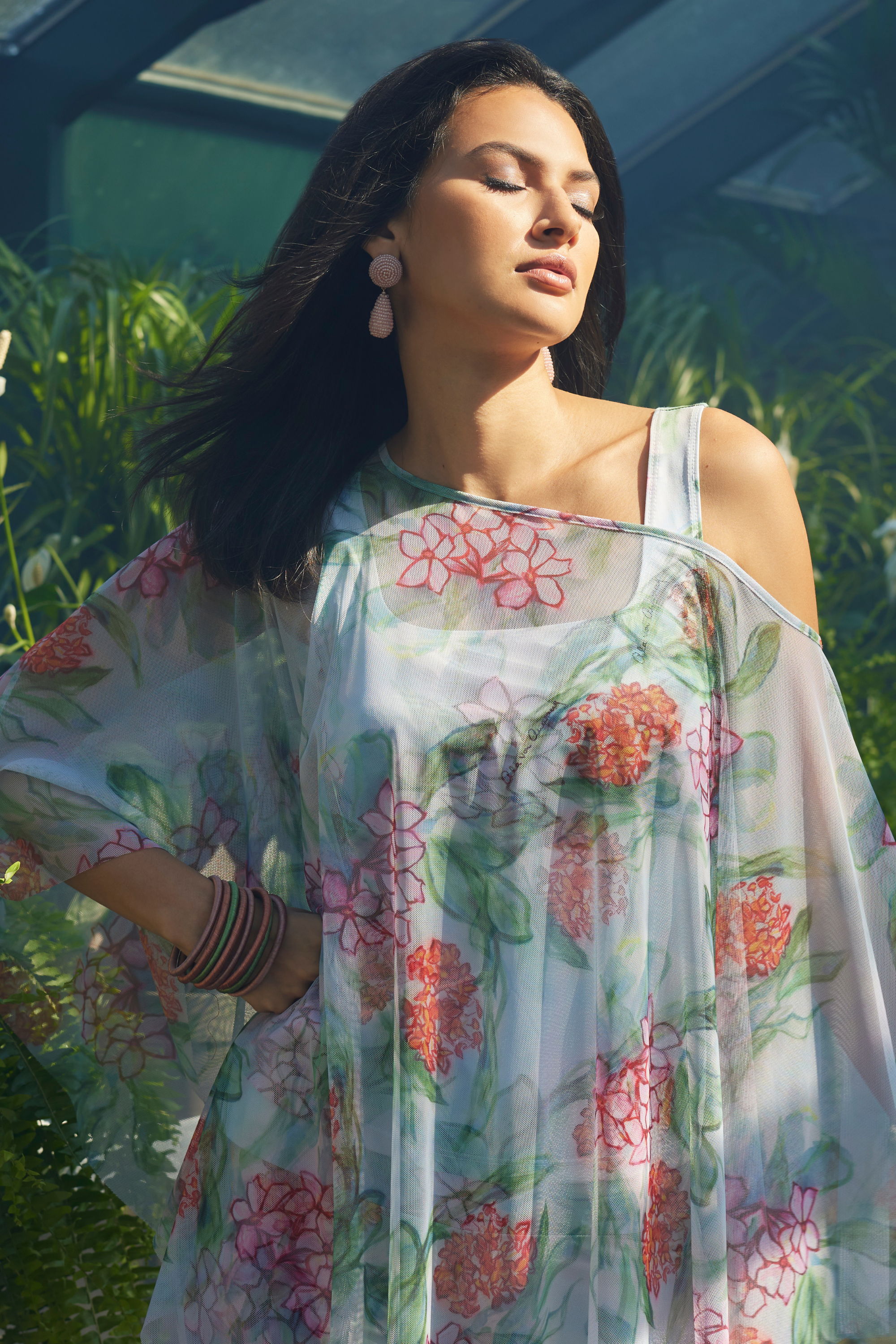 Woman in floral dress posing gracefully in a lush garden setting.