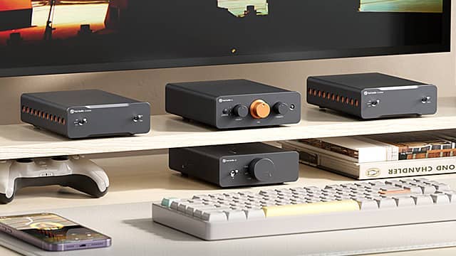 Four audio devices arranged on a shelf next to a keyboard and magazines.