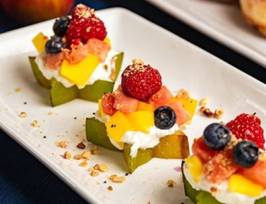 Colorful fruit cups topped with berries and cream on a white plate.