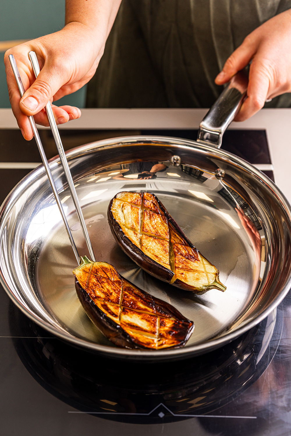 Hands holding tongs over a 316 Series Frying Pan with grilled eggplant slices.