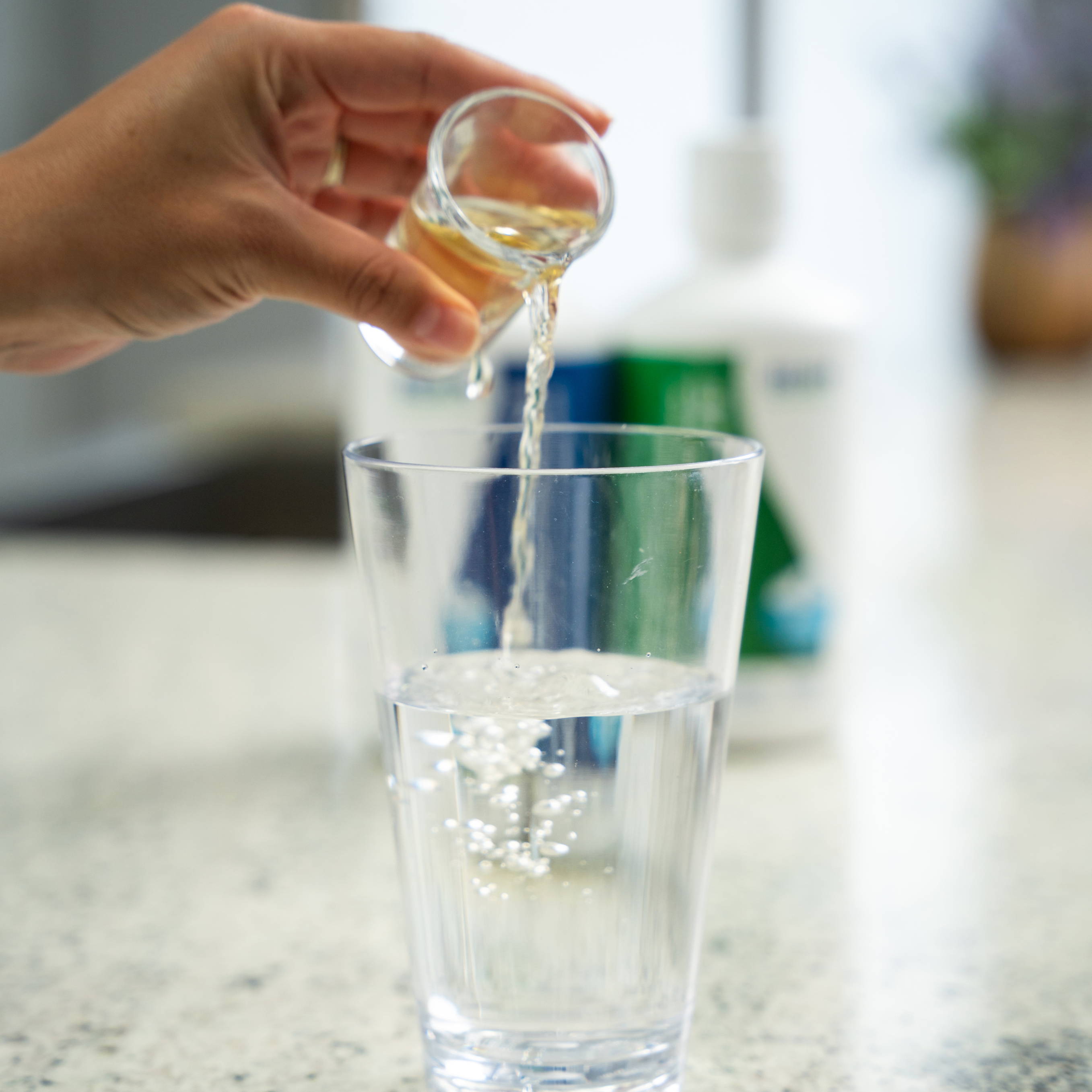 A hand pouring Electrolyze into a glass of water on a countertop.