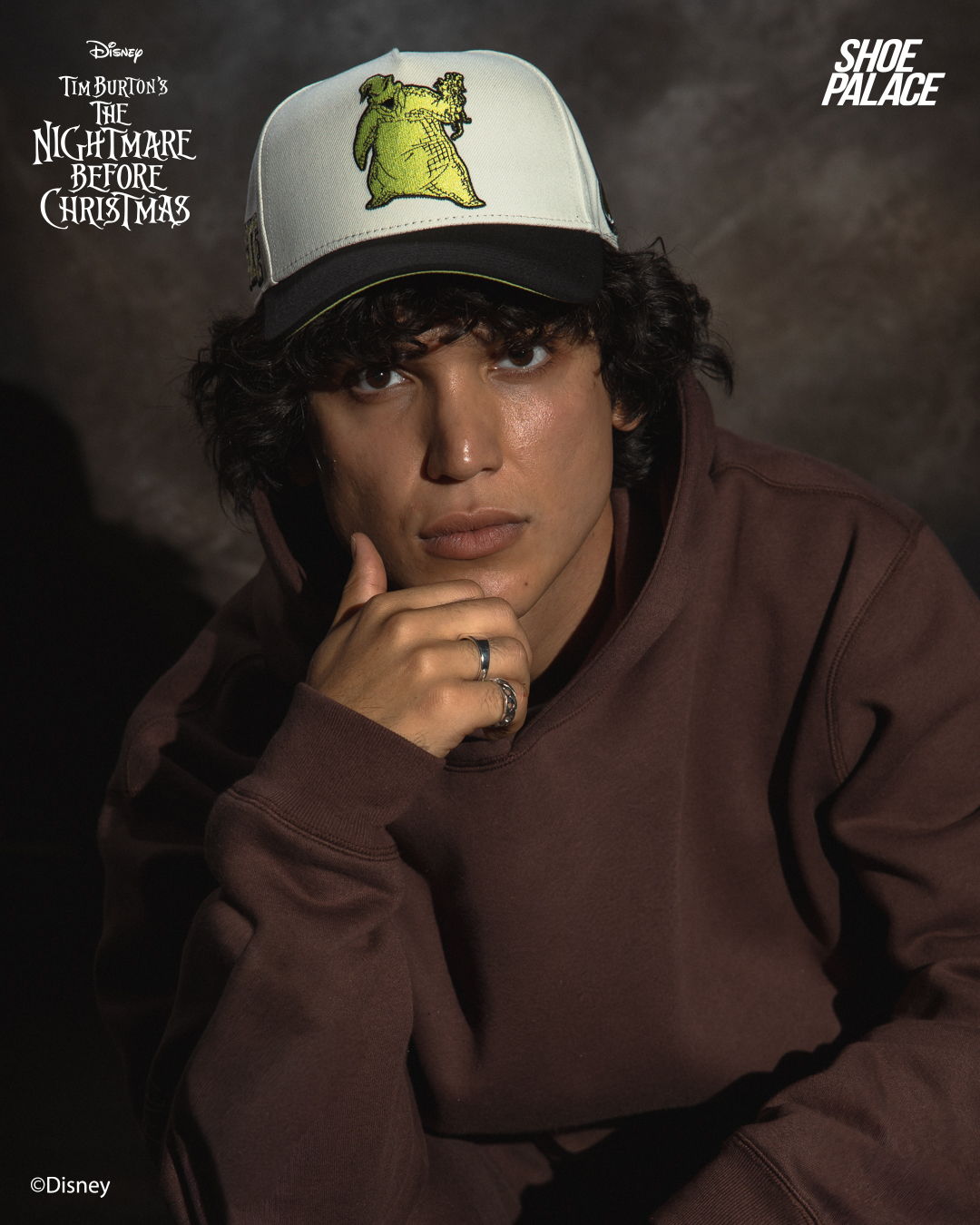 Person wearing a hat with a character, posing in a dark setting.