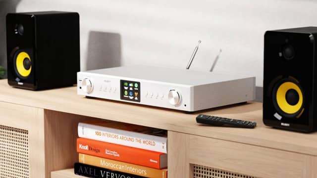 A white tuner with black speakers on a wooden shelf.