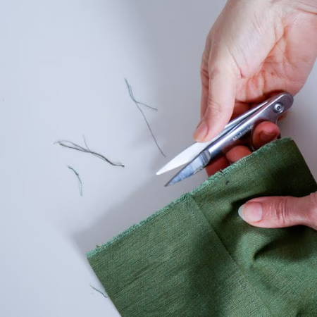 Thread snips used to cut threads off of a green fabric
