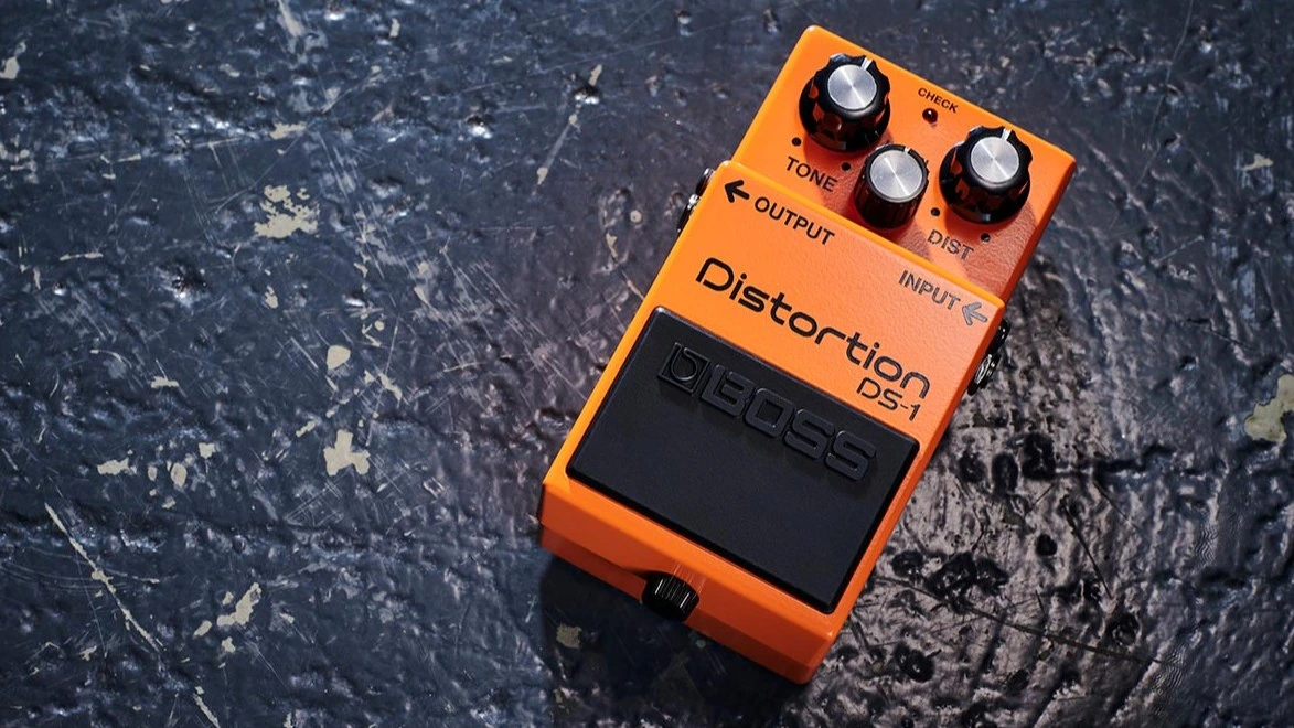 An orange guitar distortion pedal on a textured surface.