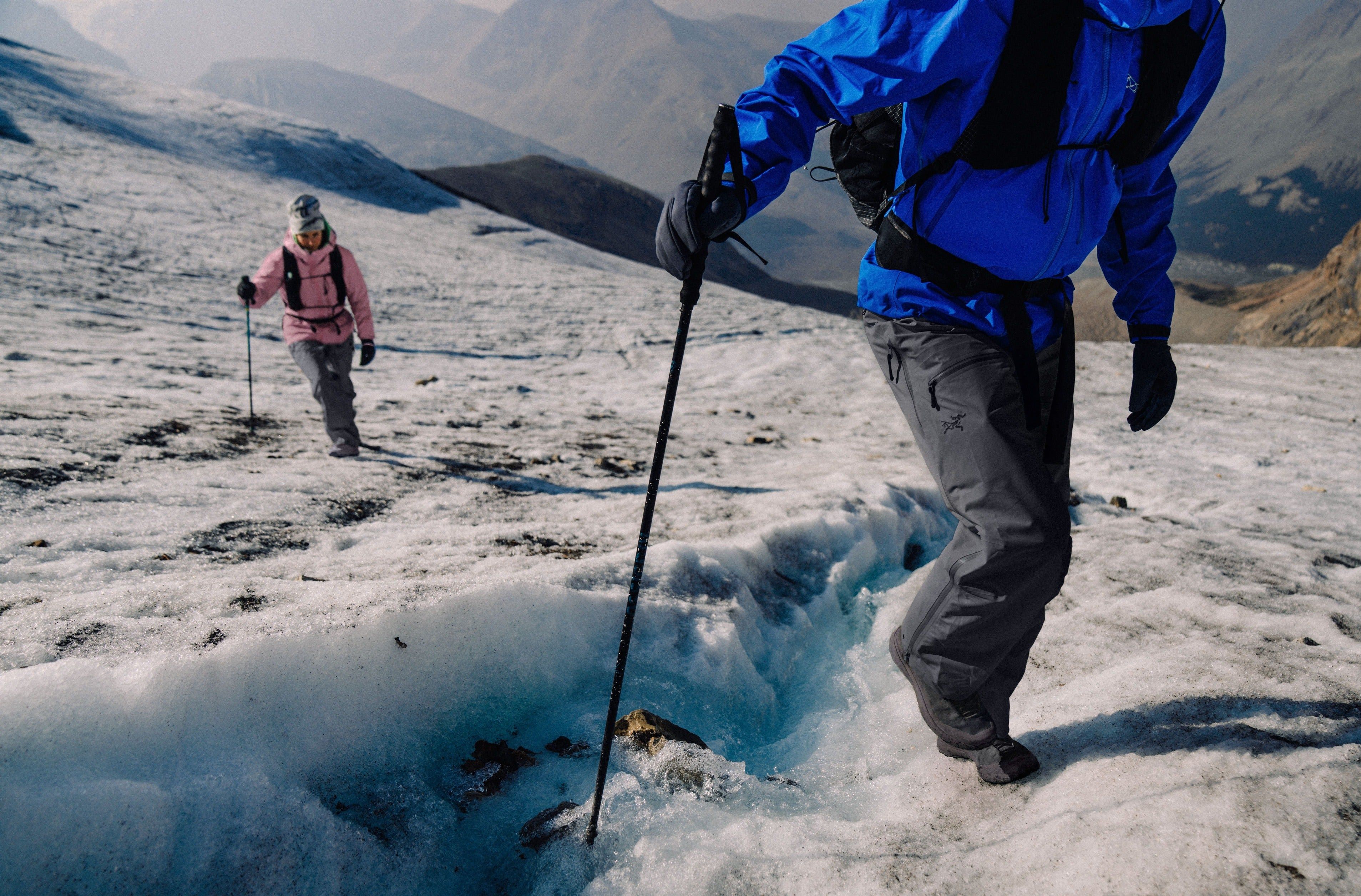 Two people hiking on a glacier with trekking poles.
