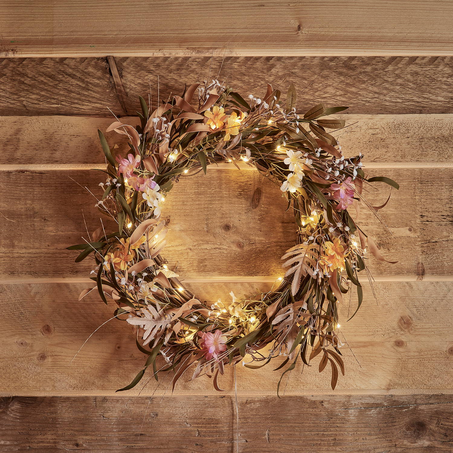 Forged flower wreath with warm white micro-lights against a wooden background.