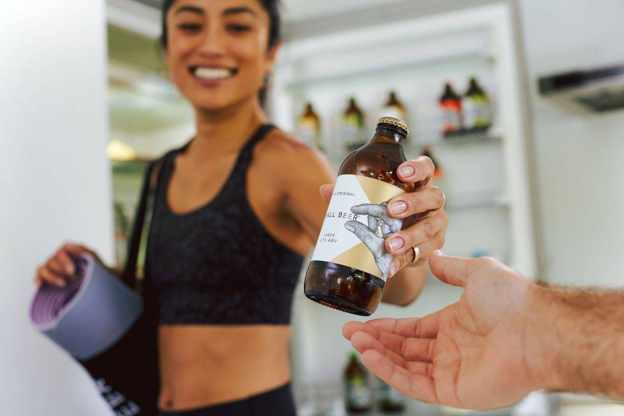 A young adult woman holding a bottle of beer after exercise