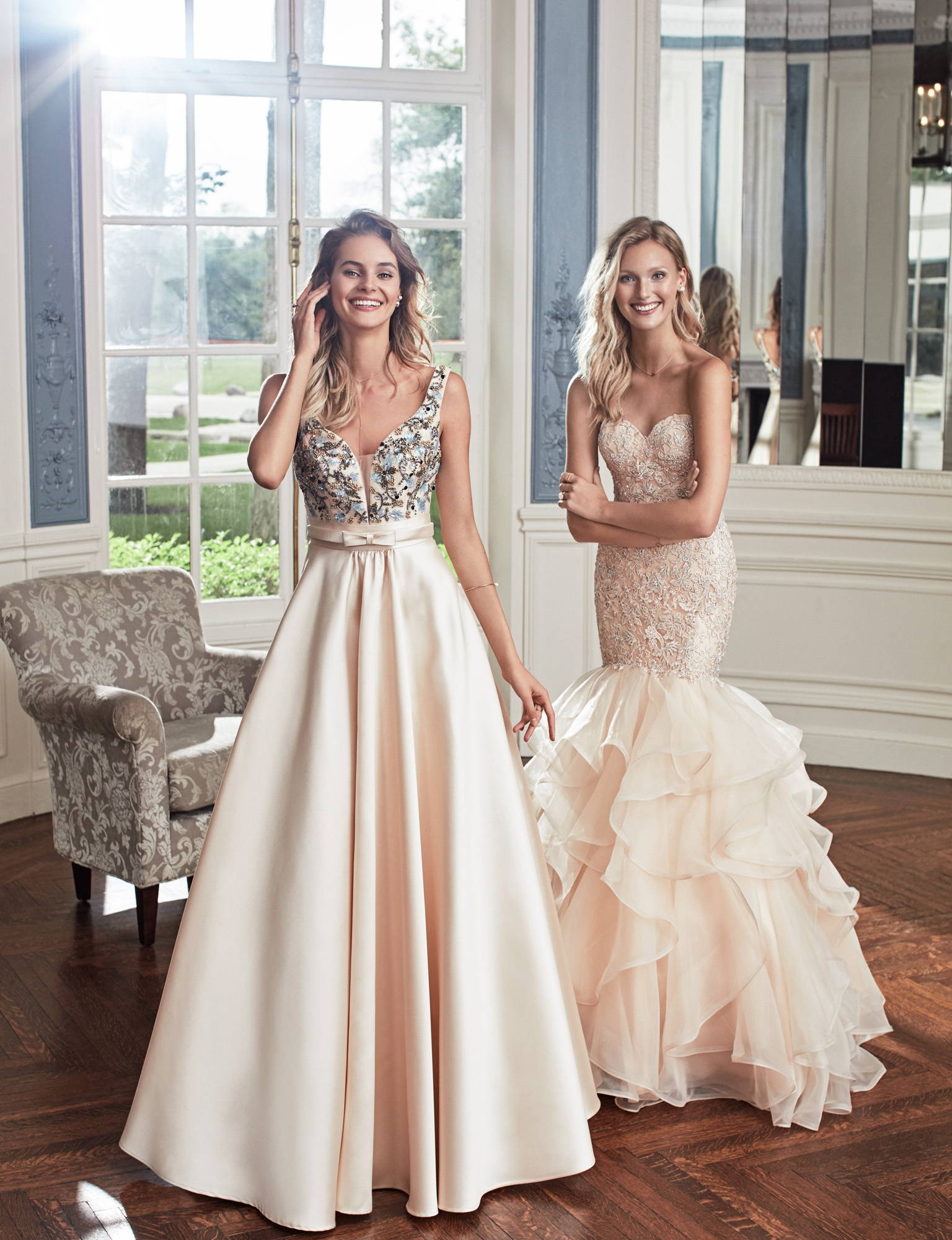 Woman wearing a cream a-line satin ball gown stands with a woman wearing a cream ruffled mermaid gown, Prom Dresses