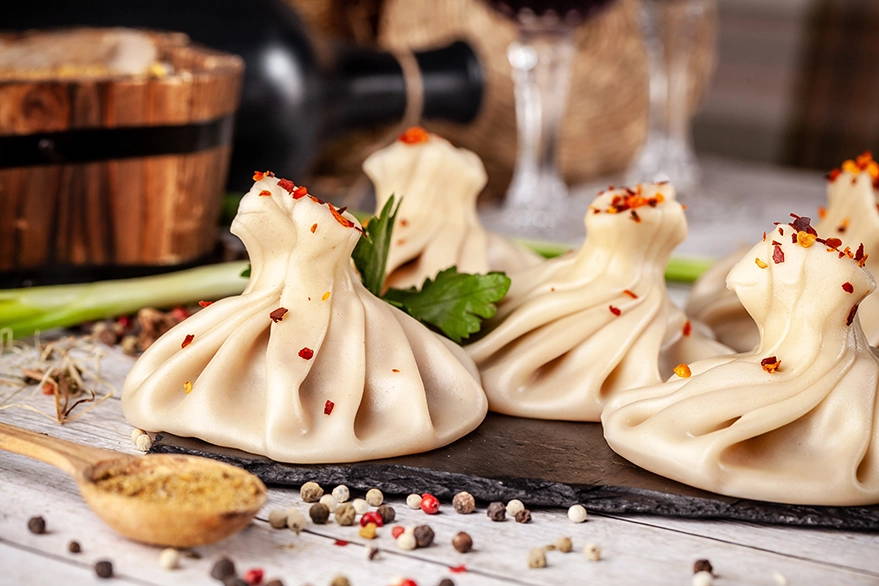 Georgian khinkali, meat dumplings sprinkled with spices and mint, presented on a slate board for a traditional meal.
