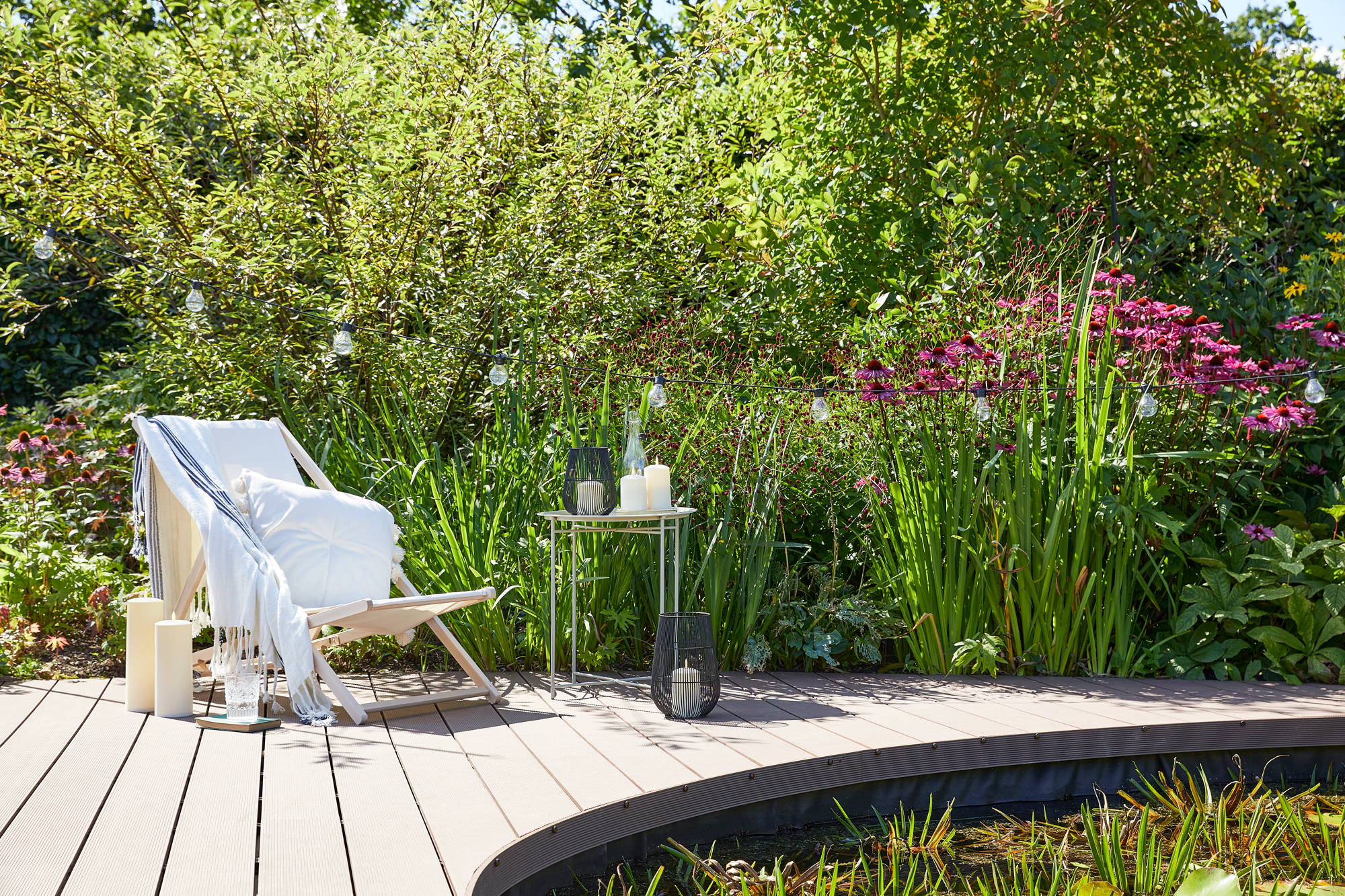 Garden setting with deck chair, pond and bushes featuring lanterns, LED candles and festoons