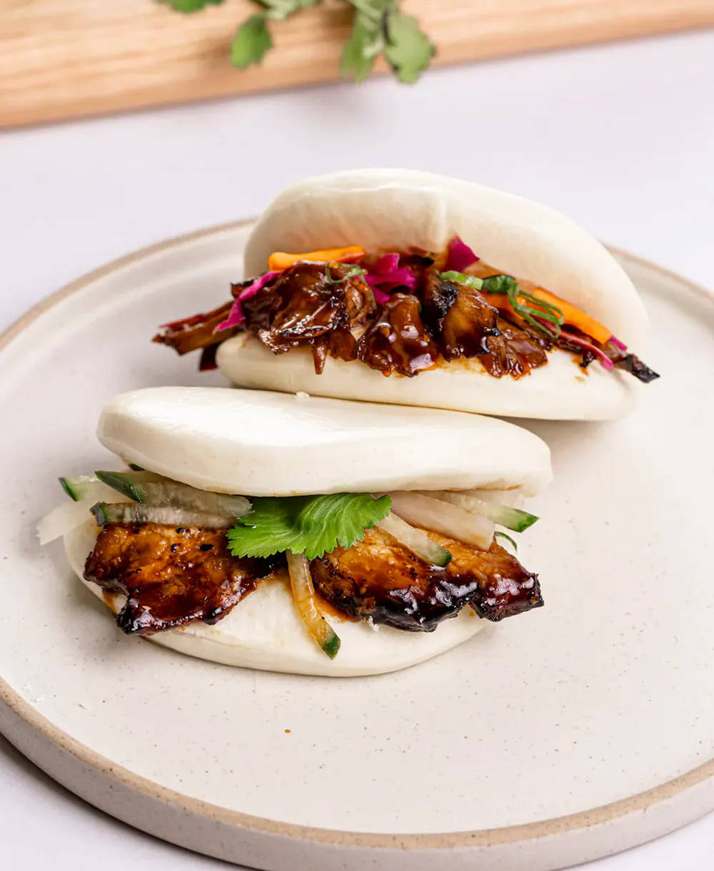 Two bao buns filled with pork and colorful vegetables on a plate.