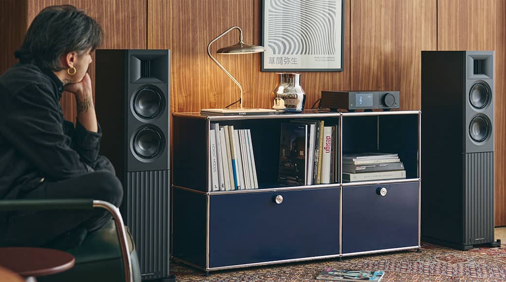 A person sitting near speakers and a modern cabinet in a stylish room.