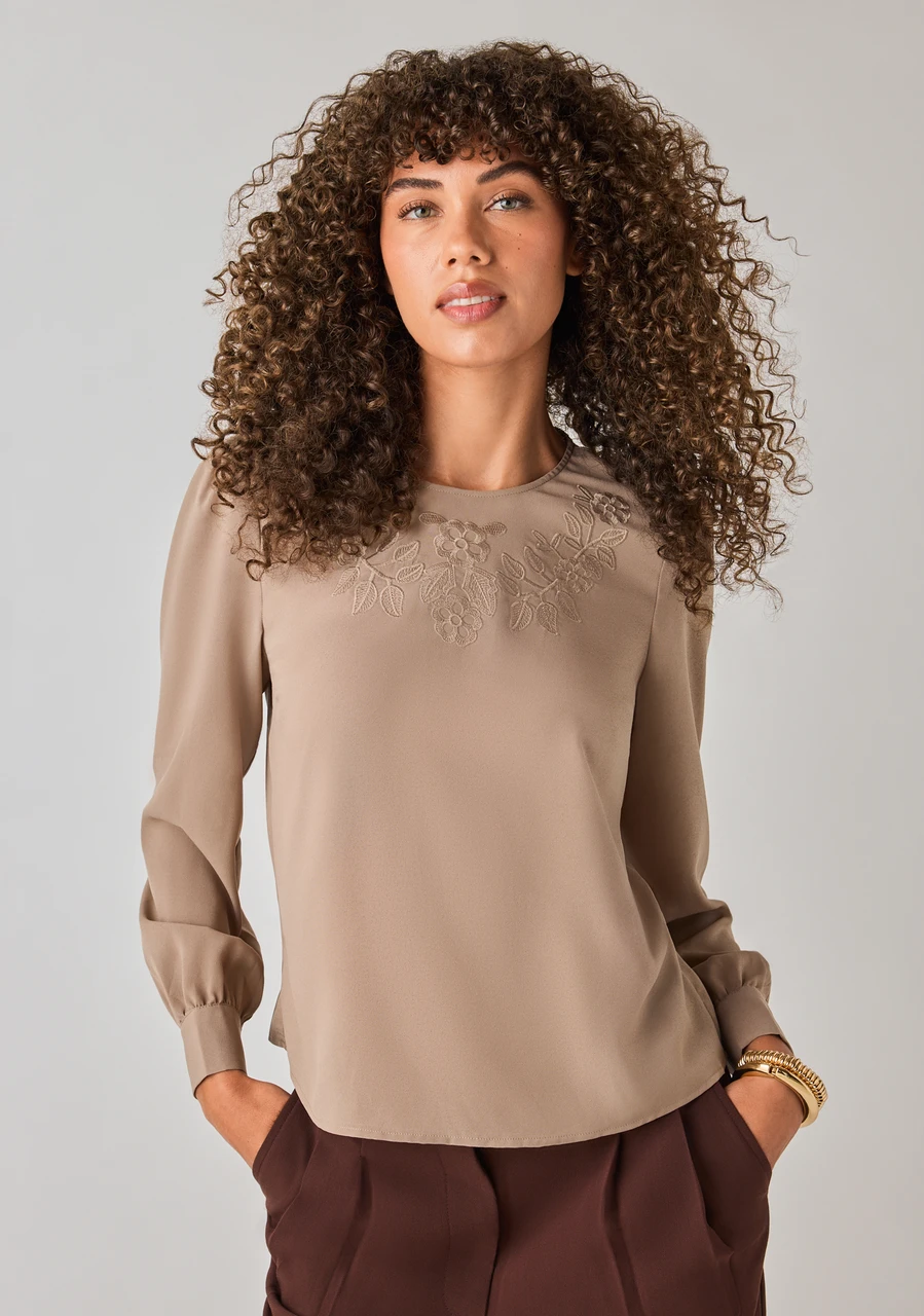 A woman with curly hair wearing a beige blouse and brown pants.