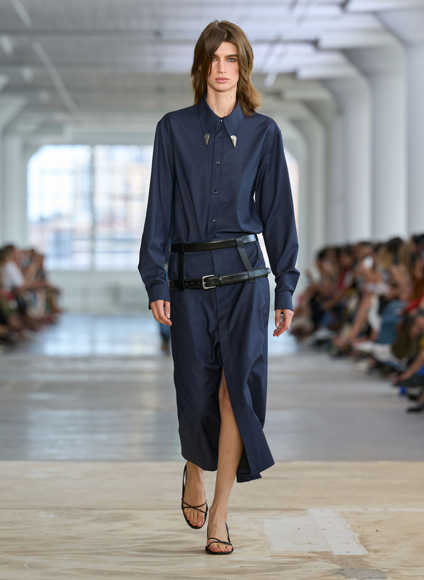 A model walking down a runway in a navy blue dress.