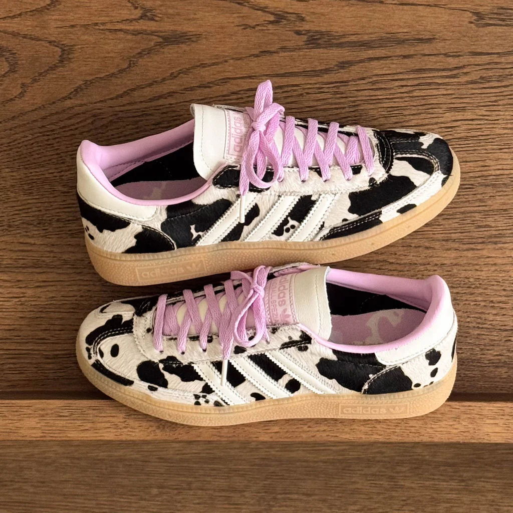Black and white cow print sneakers with pink laces on a wooden surface.