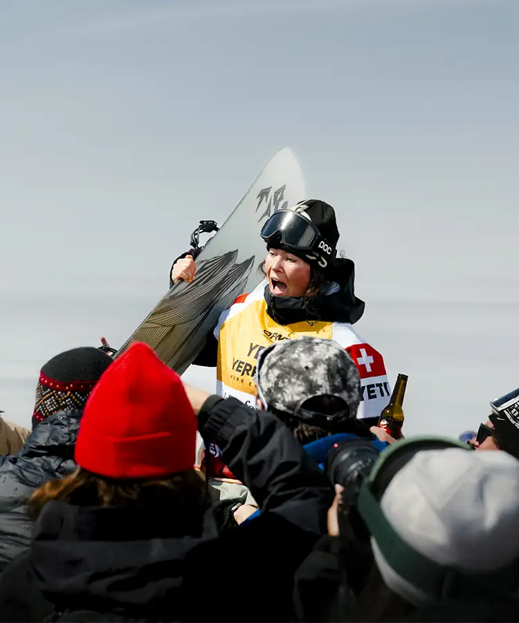 Snowboarder celebrating with a crowd, holding a snowboard in victory.