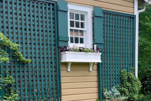 A house exterior with green shutters, window box, and lattice panels.