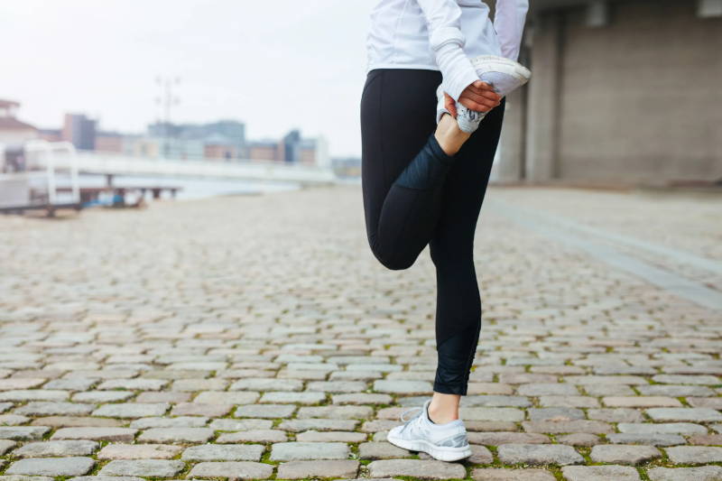 young woman stretching her thigh in before running on cobblestone street.