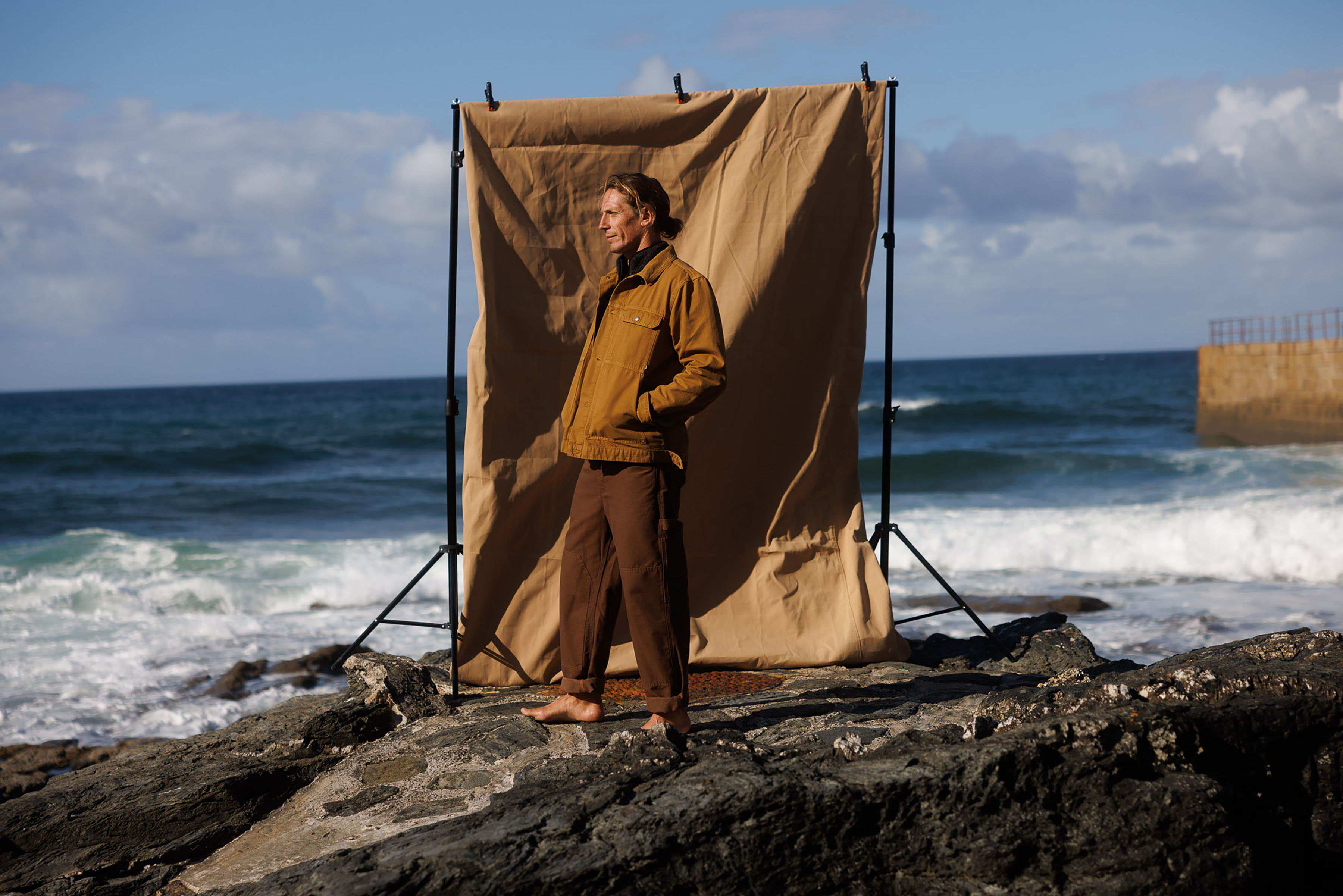 Person standing on rocks by the ocean in front of a backdrop.