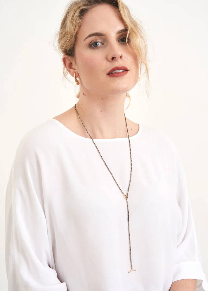 A model wearing a white top with a long beaded necklace with t-bar clasp