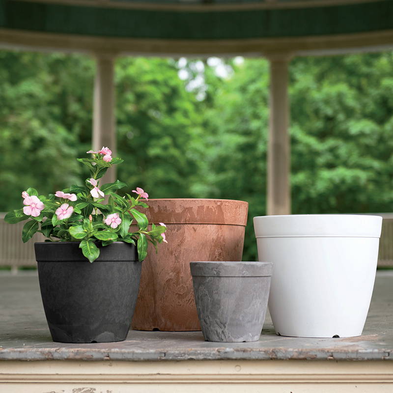Various sizes and colors of the Dolce Round Planter with pink flowers growing in the black one
