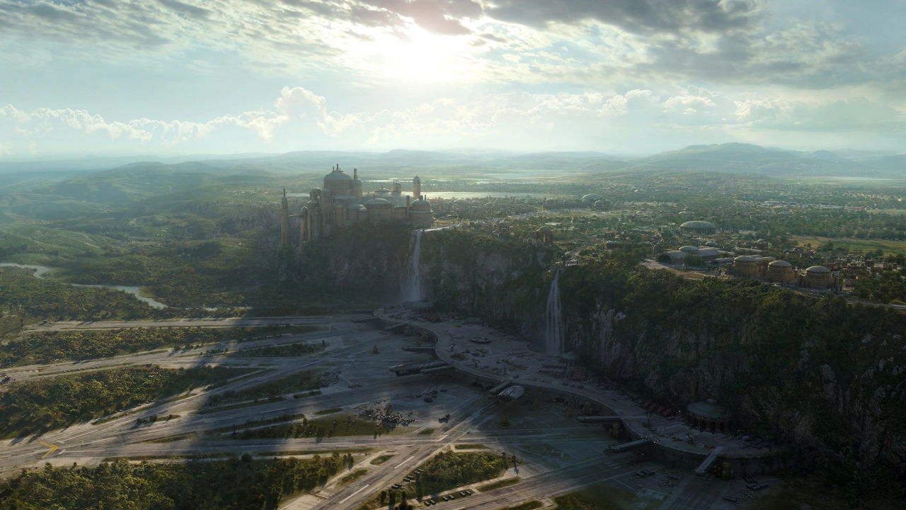 Aerial view of a castle near a river and mountains under a cloudy sky.