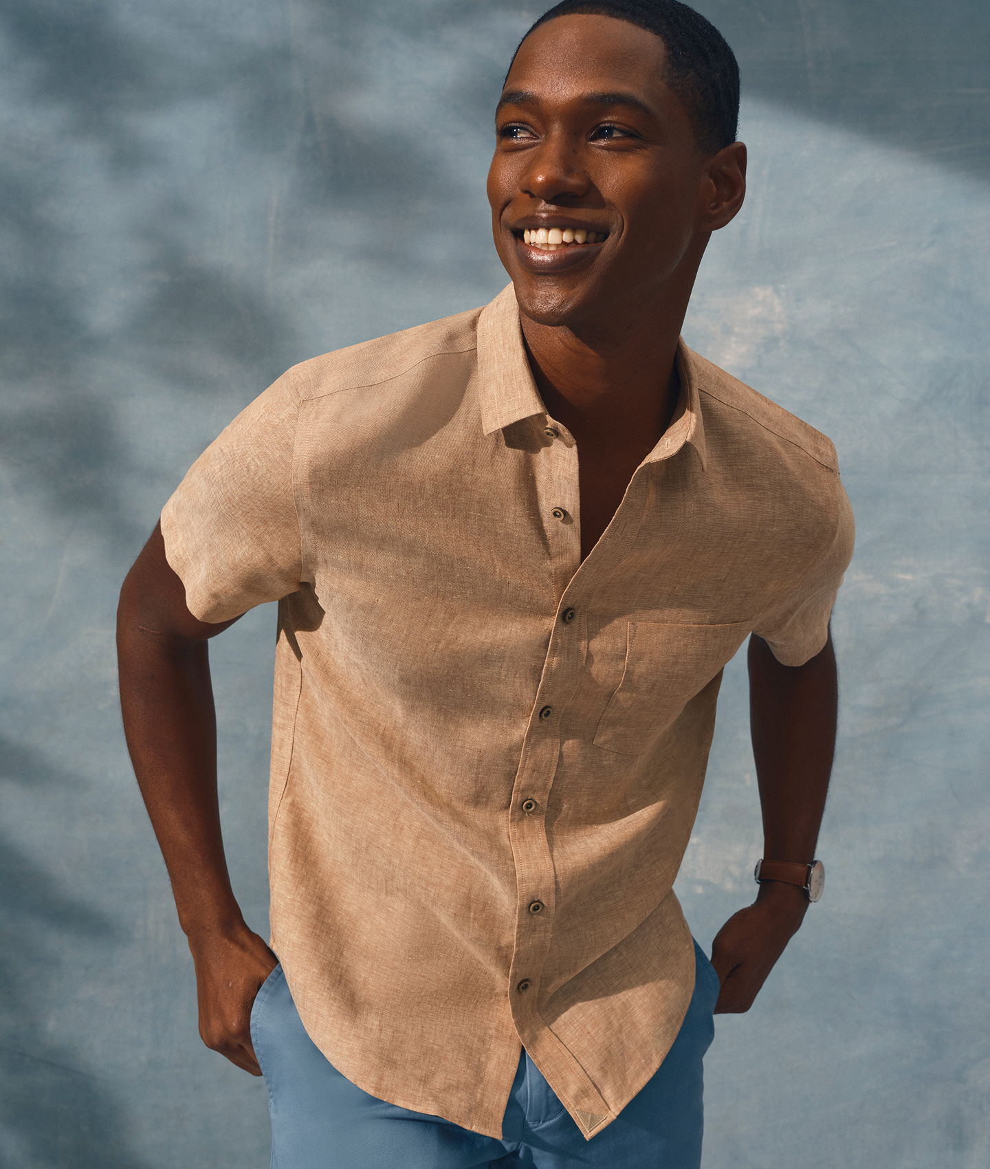 Smiling man in a short-sleeve shirt against a blue background.