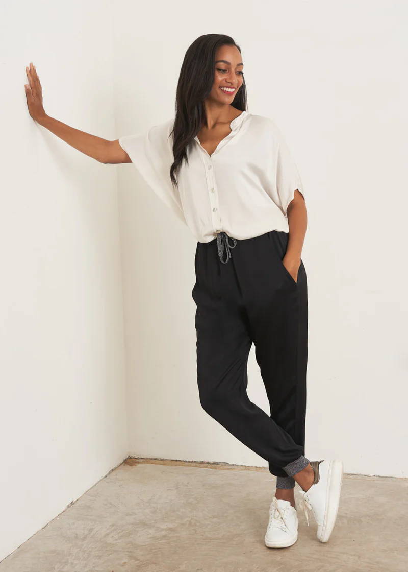 A model wearing a off white shirt with black satin trousers with glitter drawstring and matching ankle cuffs with white trainers