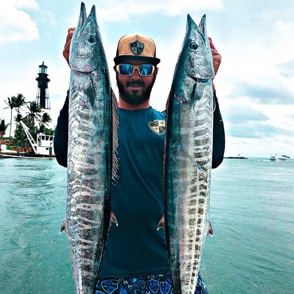 Phil Alves holding up two large fish to the camera while wearing an SA Company hat, sunglasses and an SA Company performance shirt.
