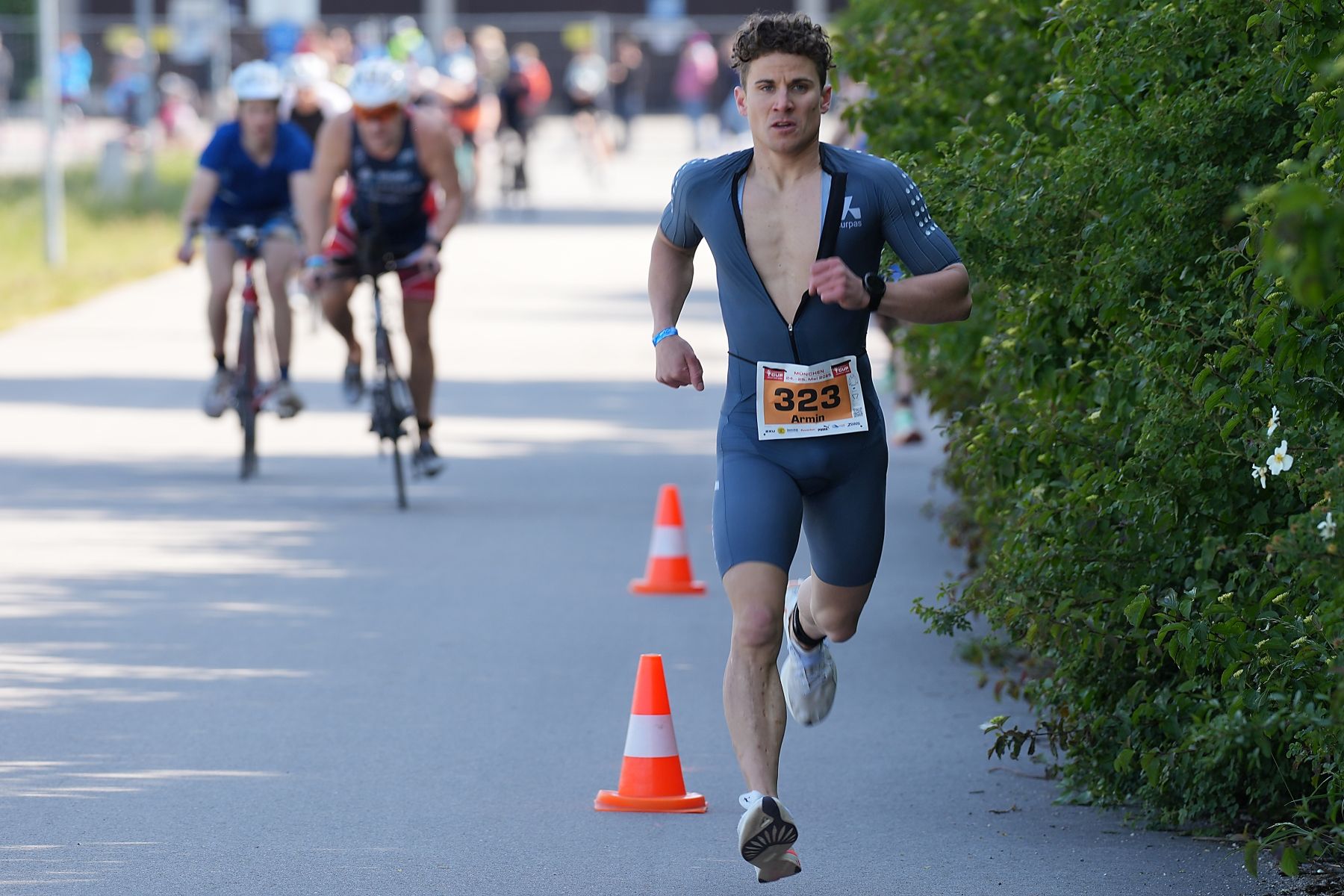 Ein junger Triathlet auf der Laufstrecke, neben ihm Radfahrer