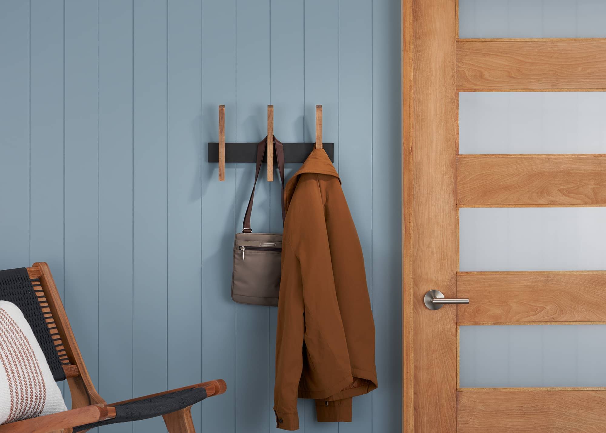 wall rack with 3 wooden hooks on a wall with a sling bag and coat hanging on it