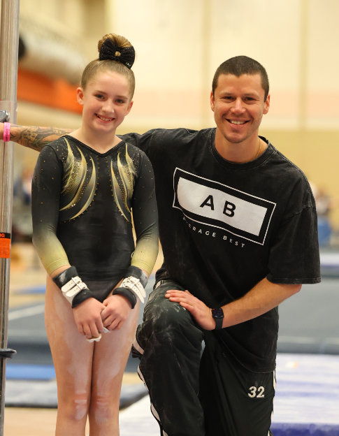 A gymnast poses with her coach, both smiling at the camera.