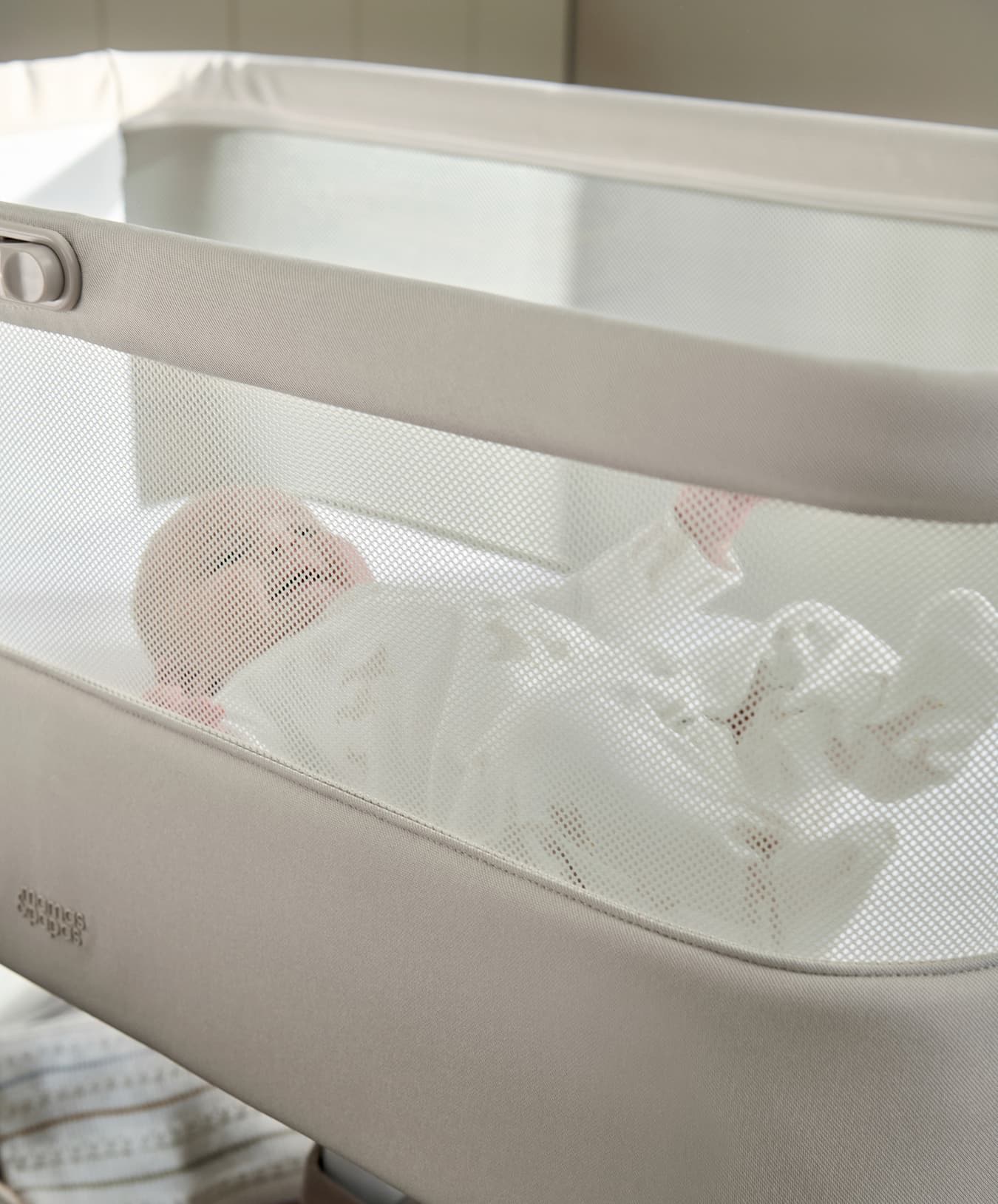 Baby sleeping in a modern bassinet with a mesh cover.