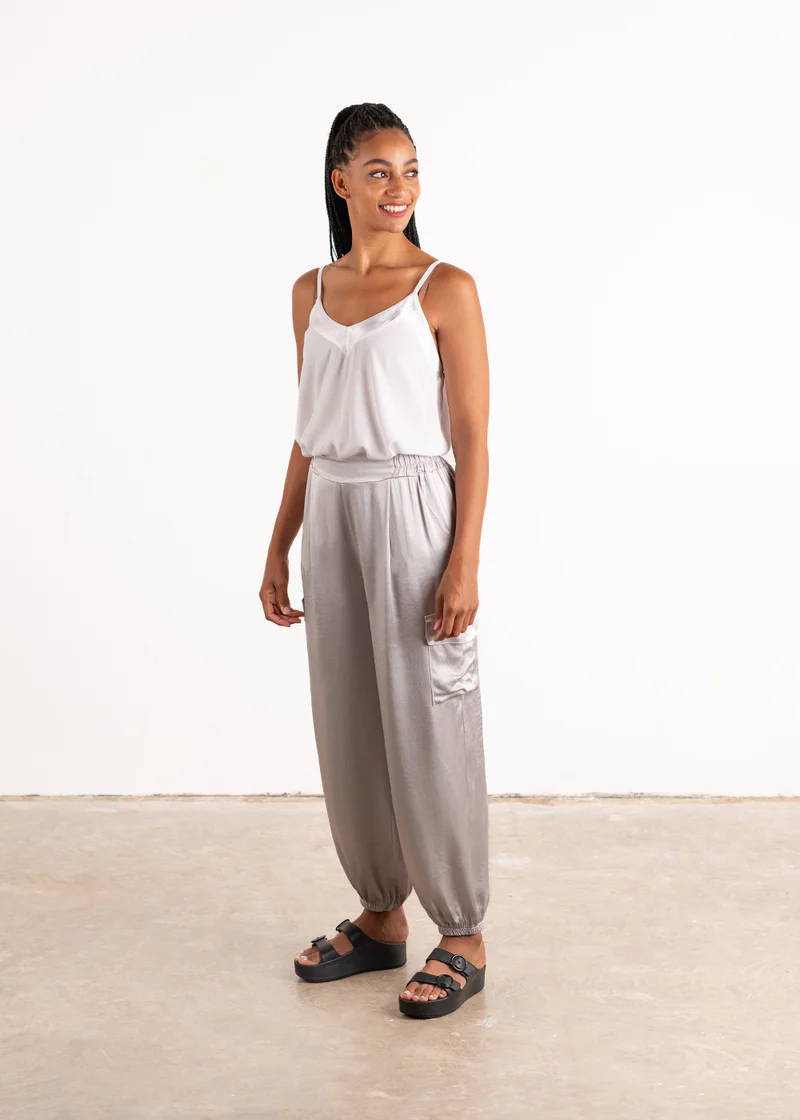 A model wearing a pair of silver, satin cargo trousers with a white strappy top and black chunky platform slides
