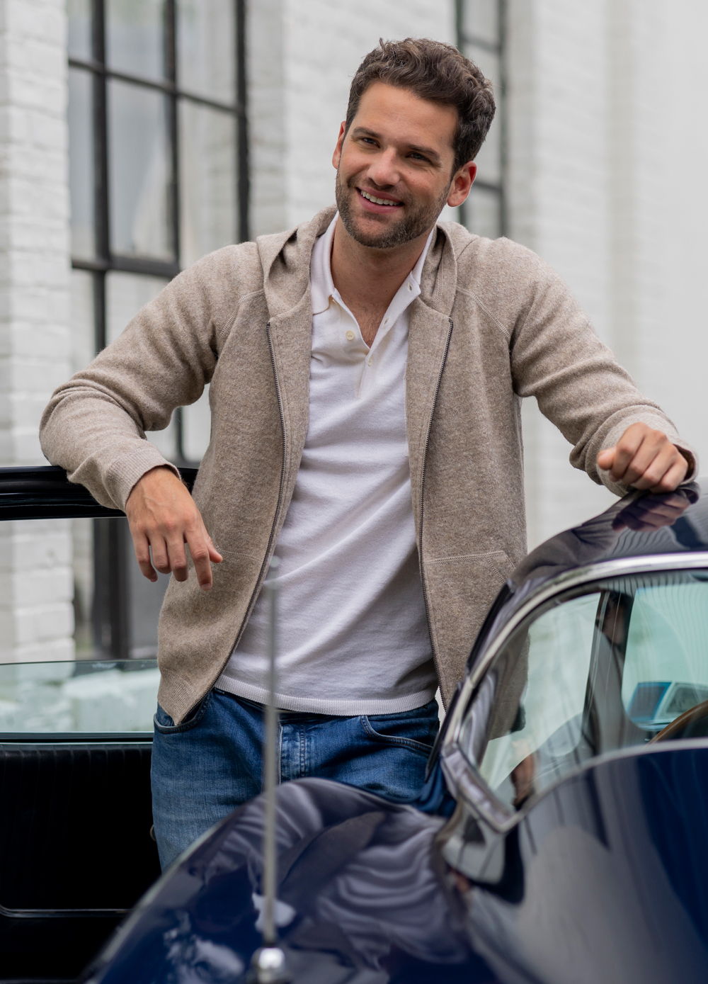 Smiling man in casual attire leaning on a classic car.