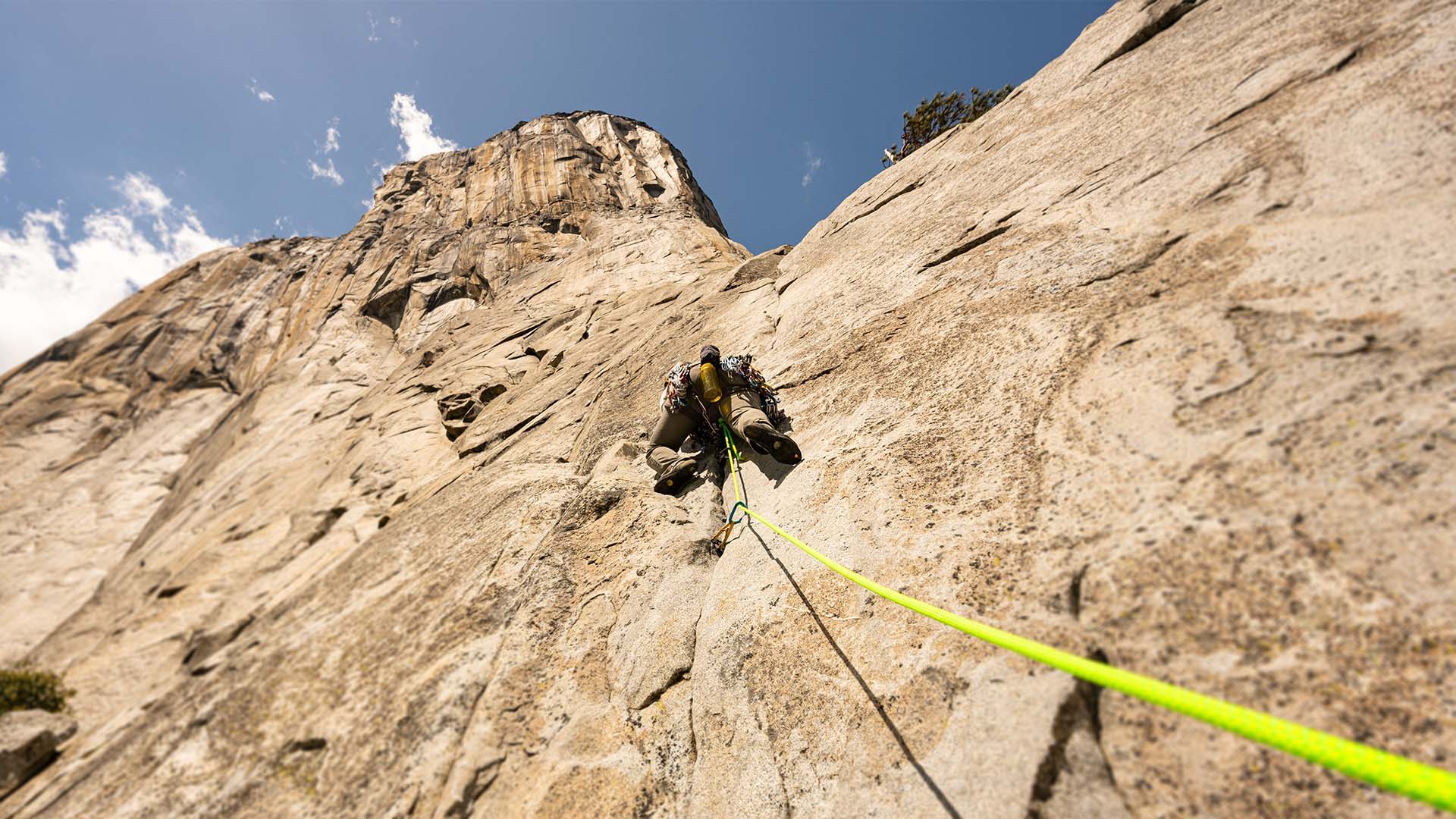 Climber ascending a rock face with a rope against a blue sky.