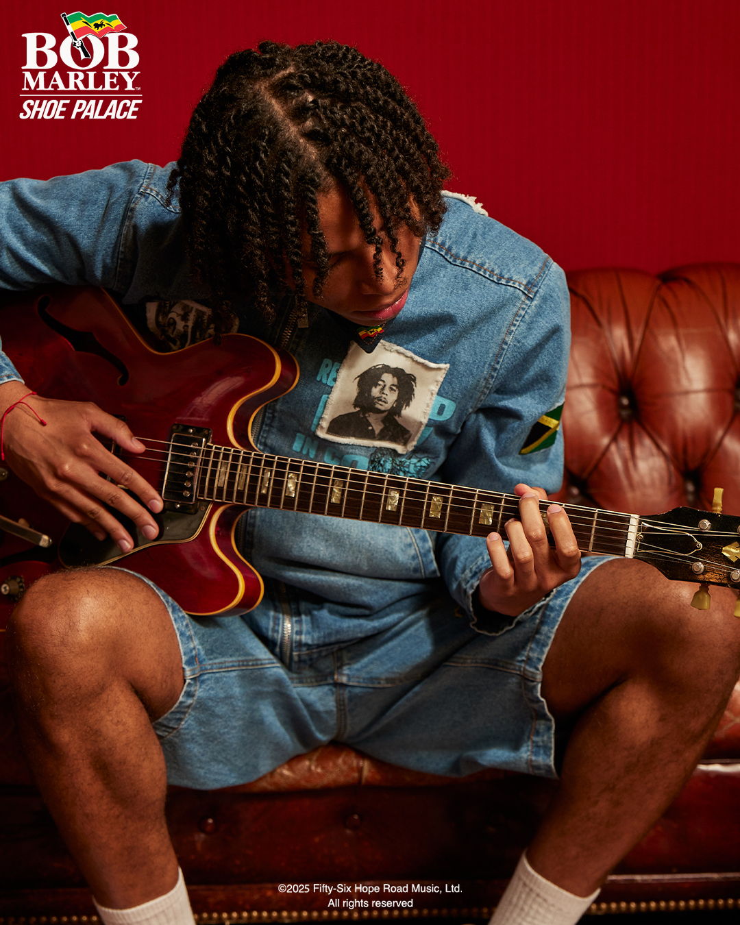 Person sitting on a couch playing a guitar, wearing a denim outfit.
