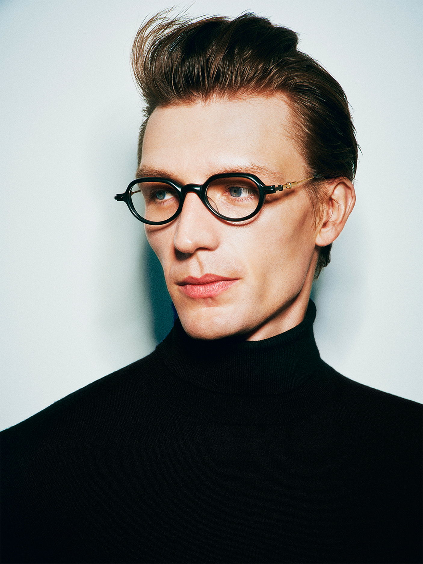 A man wearing Robert Marc glasses and a black turtleneck, looking thoughtfully.