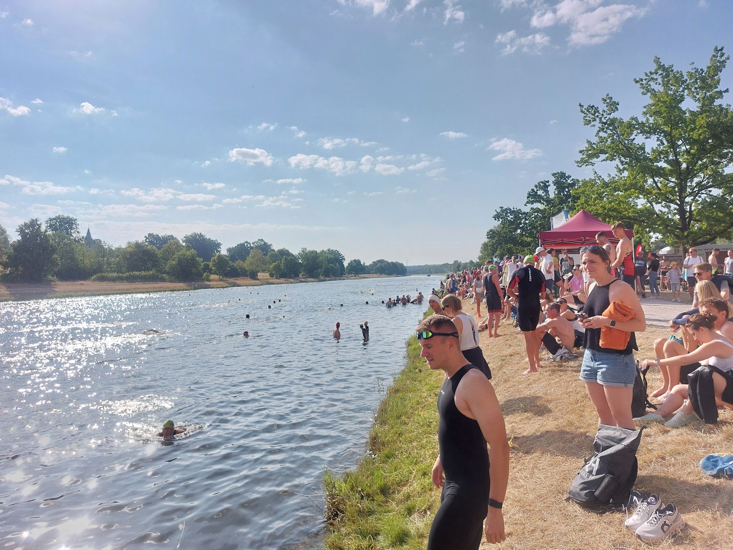 Fans eines Triathlons stehen am Rand des Ufers und feuern die Schwimmer an.