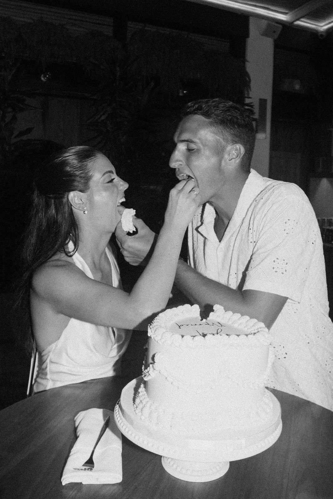 Couple playfully feeding each other cake at a celebration.