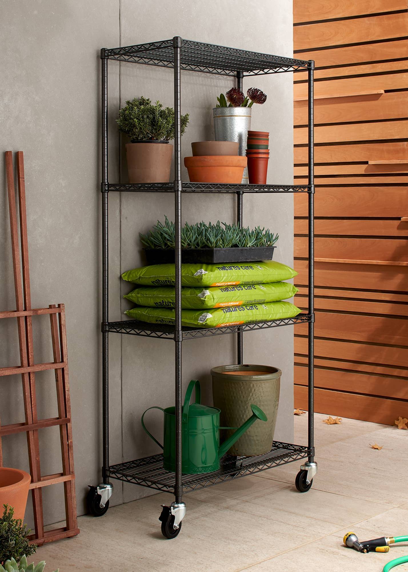 black outdoor wire shelving rack filled with gardening tools and supplies