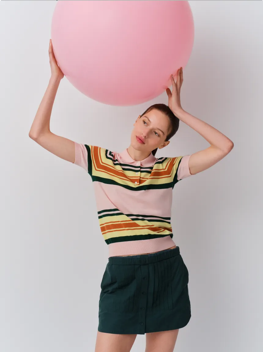 A woman holding a large pink balloon, wearing a colorful striped shirt and shorts.